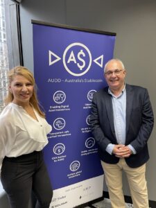 Picture of David Birch and Effie Dimitopoulous standing in front of the Novatti banner on his Digital Identity Tour