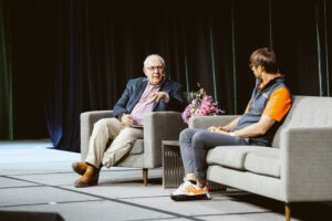 David Birch on stage with Jonny Ayers, both sat in armchairs on the stage