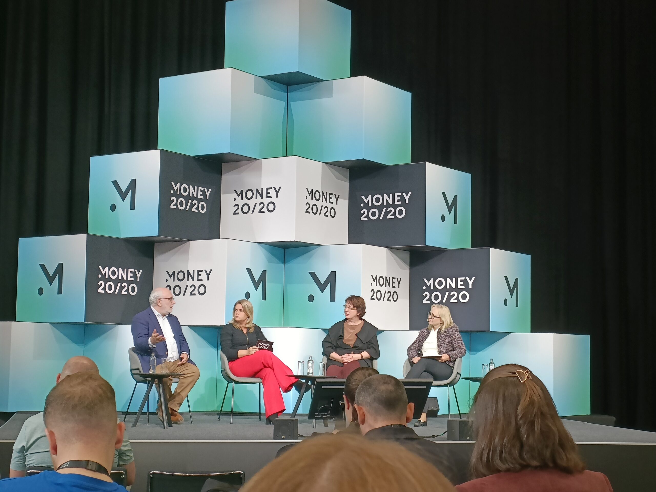 Moderating at Money 20/20 Europe 2025: Do I Have The Right To Be A Dog Online? David Birch on stage with fellow panellists on the SUmmits stage with a pyramid of cubes stacked behind them on stage with the Money 20/20 logo on them.